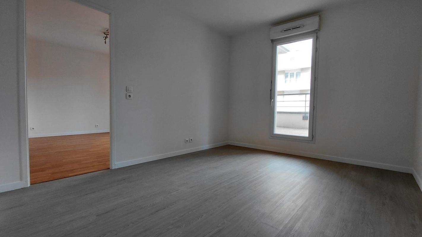 Photo 12 : chambre sol stratifié gris, fenêtre simple sur terrasse, accès au séjour par une porte, murs blancs, état neuf
