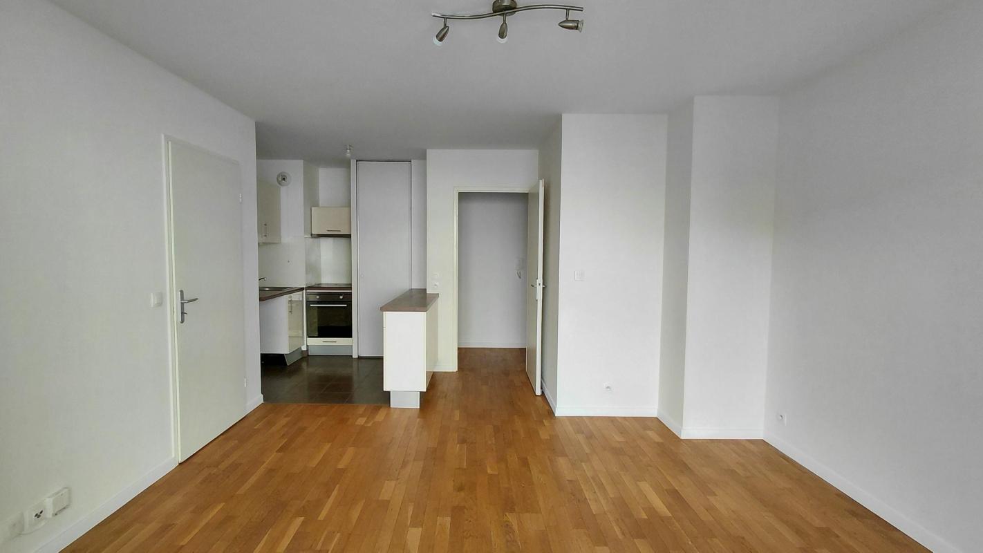 Photo 8 : cuisine ouverte compacte blanche et bois, four encastré, sol sombre, séjour d’environ 20 m²